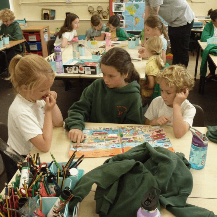 Schoolchildren seated around tables, reading a book